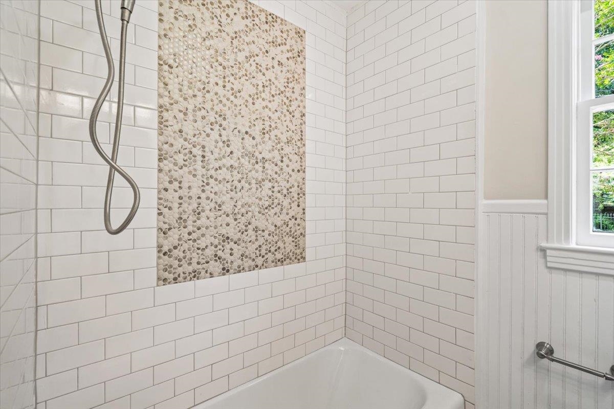 170 South Greer Street Memphis, TN 38111 - Photo 10 of 35 Bathroom featuring a subway tile shower surround with a mosaic accent wall, white tub, and a window with trim