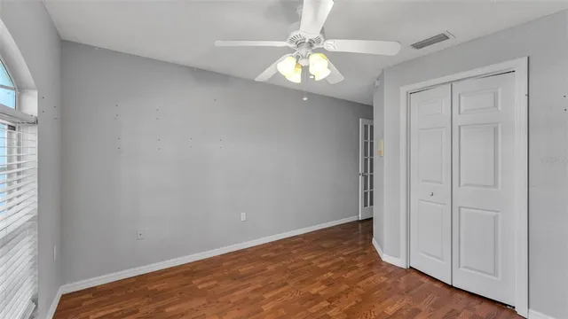 an empty room with wooden floor chandelier fan and windows