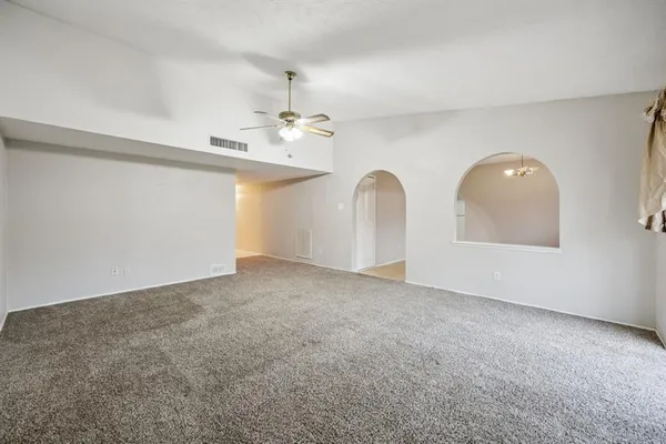 an empty room with chandelier fan and windows