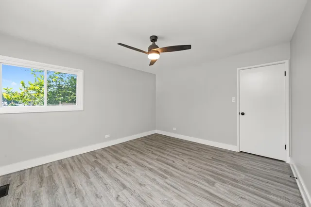 an empty room with wooden floor ceiling fan and windows