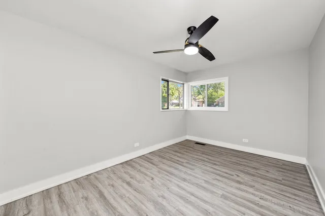 an empty room with wooden floor fan and windows