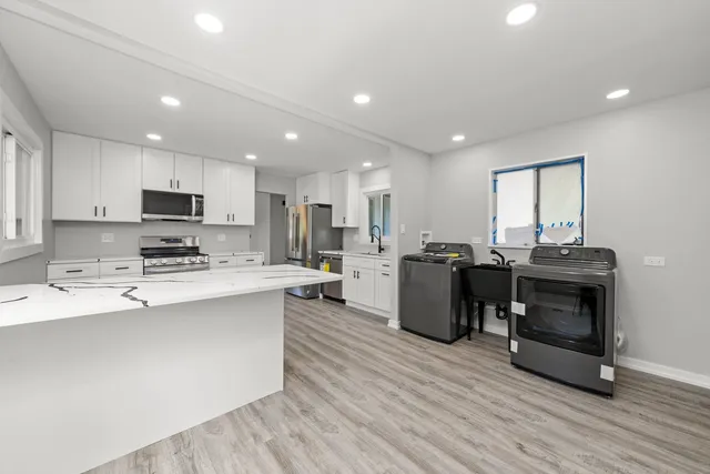 a kitchen with stainless steel appliances a stove a sink a refrigerator white cabinets and wooden floor