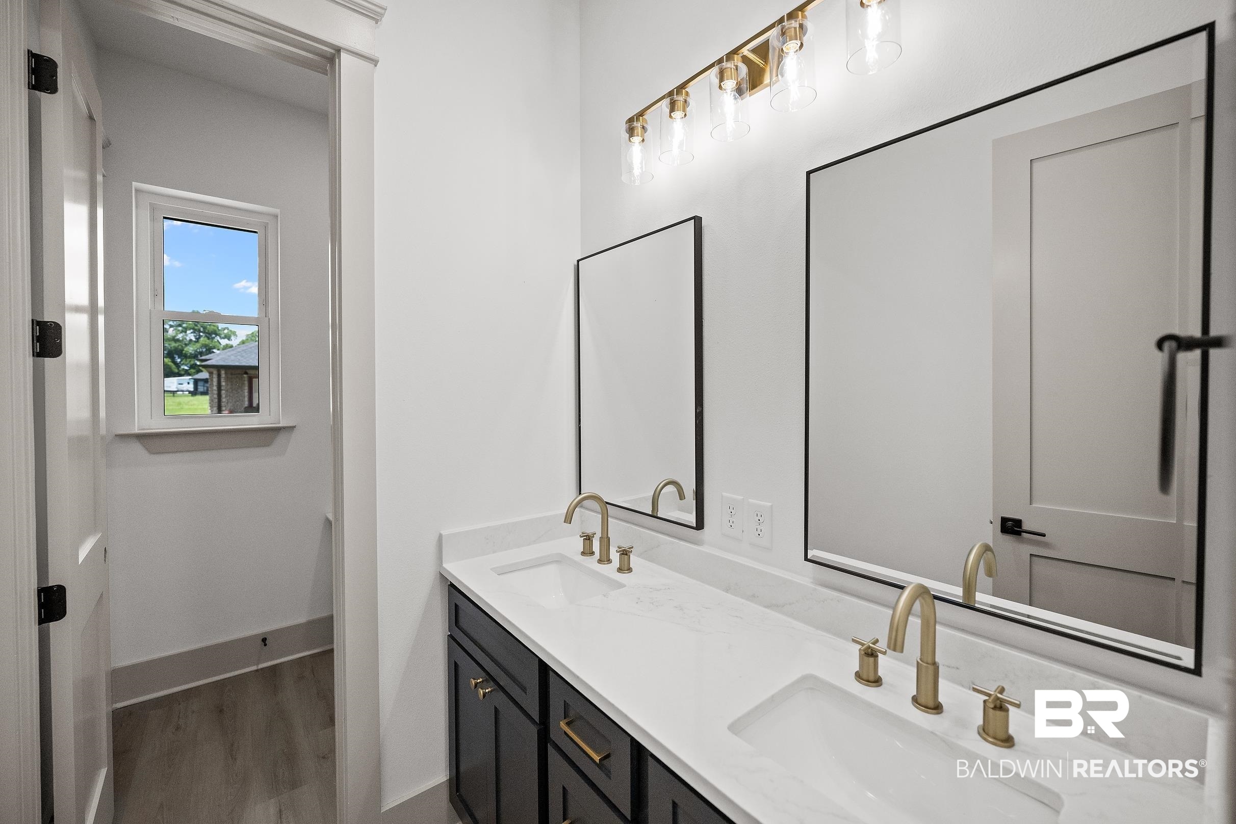 13111 Gopher Court Elberta, AL 36530 - Photo 30 of 41 Dual vanity featuring a white countertop with integrated sinks, matte gold fixtures, and black framed mirrors