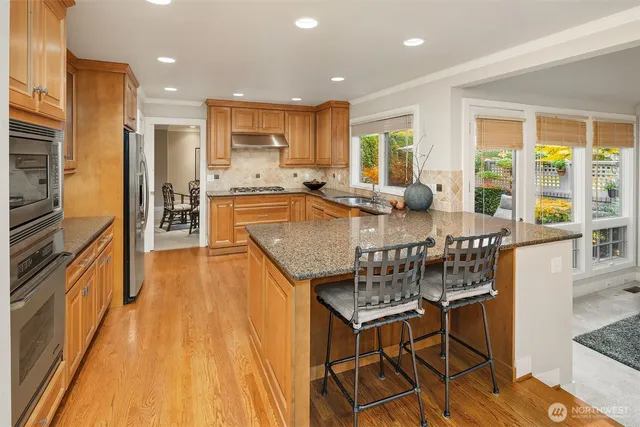 a dining hall with stainless steel appliances granite countertop a stove top oven a dining table and chairs with wooden floor