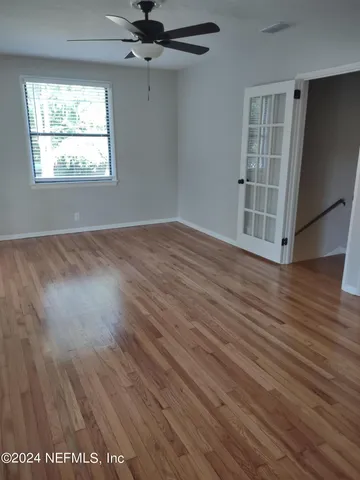 an empty room with wooden floor fan and windows