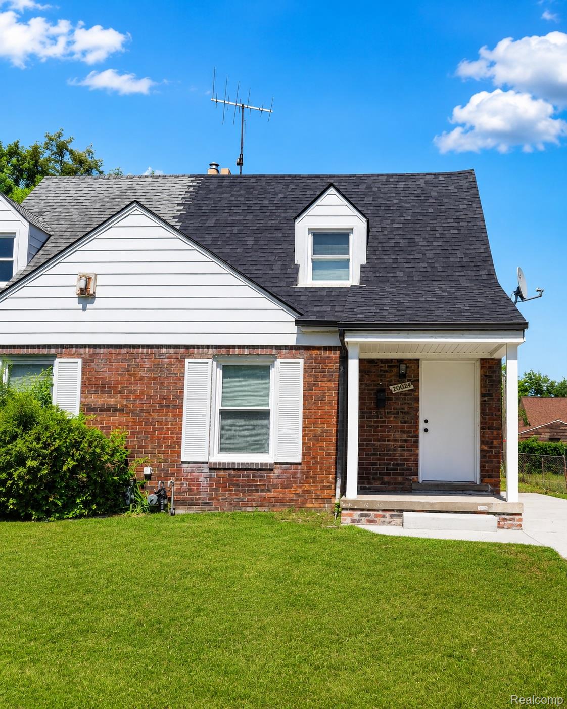 Brick facade home featuring a covered front entry, white paneled siding on the upper gable, and a dormer window