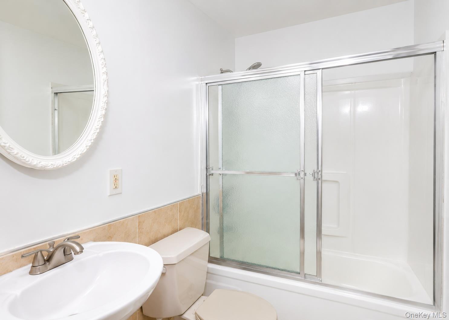 43 Glenmere Homesites Road, Unit 2F Florida, NY 10921 - Photo 8 of 15 White bathroom featuring a shower-tub combination with sliding glass doors, a pedestal sink with a brushed nickel faucet, a toilet, and a decorative oval mirror