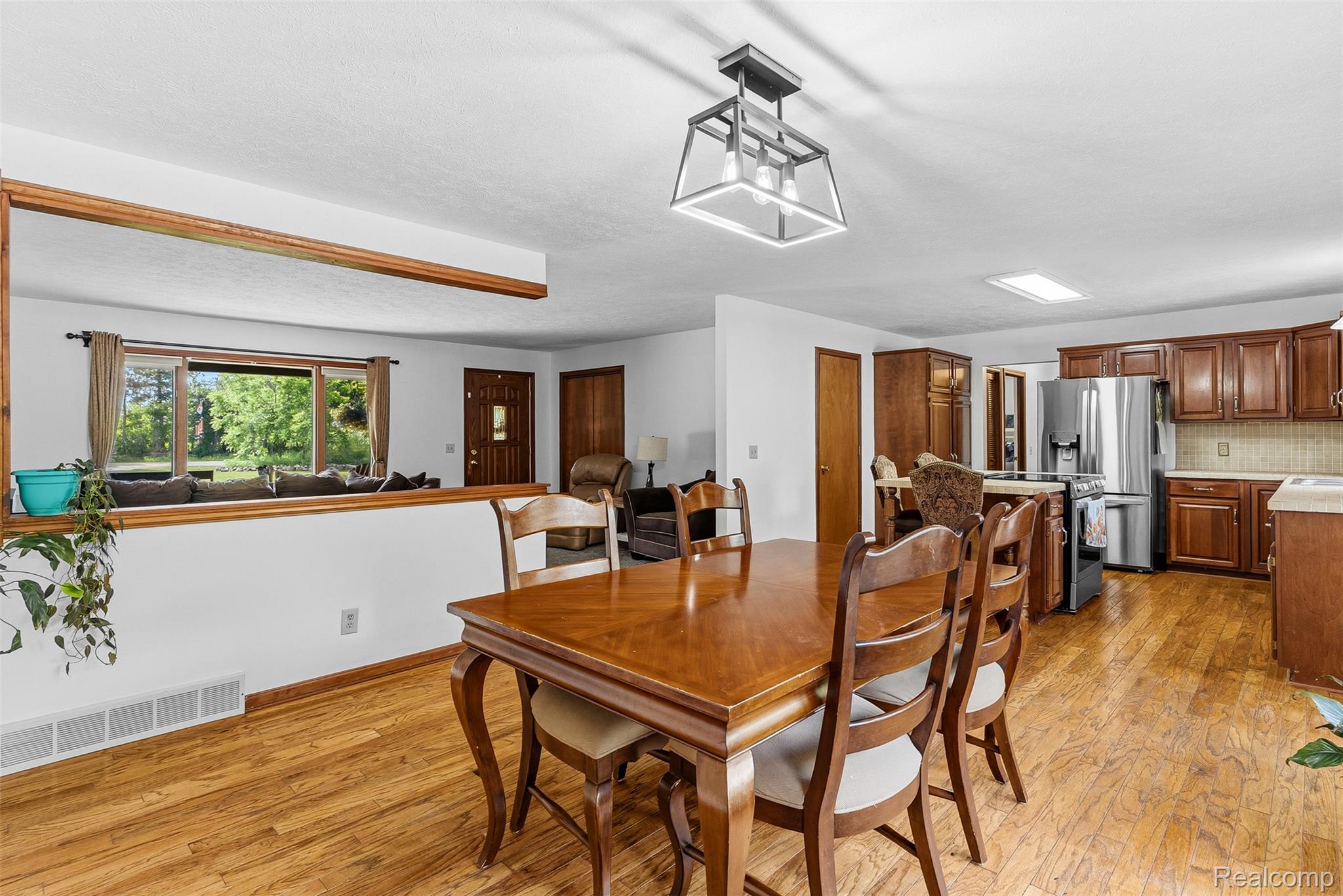 6699 Lansing Road Durand, MI 48429 - Photo 10 of 53 Kitchen and dining area featuring wood-finish flooring, dark wood cabinetry, stainless steel appliances, and a tiled backsplash