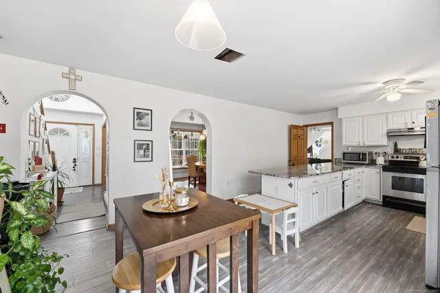 a kitchen with stainless steel appliances kitchen island granite countertop a stove a sink dishwasher a dining table and chairs with wooden floor