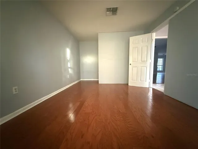 an empty room with wooden floor and windows with curtains