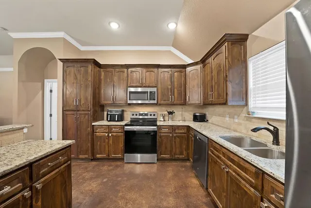 a kitchen with stainless steel appliances granite countertop a sink a stove a refrigerator cabinets and a window