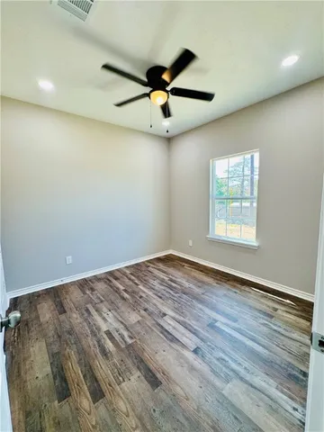 an empty room with wooden floor ceiling fan and windows
