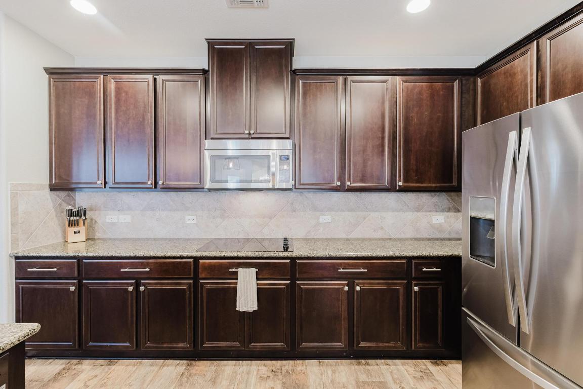 1420 Crested Butte Way Georgetown, TX 78626 - Photo 11 of 40 Kitchen with appliances with stainless steel finishes, dark brown cabinets, light stone countertops, backsplash, and recessed lighting (refrigerator does not convey)
