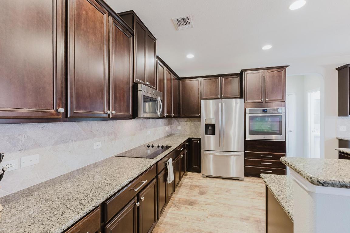 1420 Crested Butte Way Georgetown, TX 78626 - Photo 12 of 40 Kitchen with dark brown cabinetry, stainless steel appliances, light stone countertops, and recessed lighting