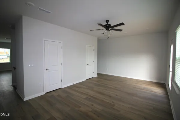 an empty room with wooden floor a ceiling fan and windows