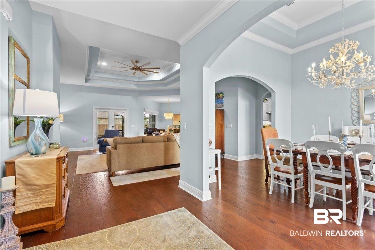 7056 Rocky Rd Loop Gulf Shores, AL 36542 - Photo 9 of 41 Living area with a tray ceiling, arched walkways, dark wood-type flooring, a chandelier, and ornamental molding
