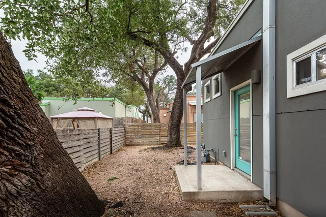 a backyard of a house with large tree and wooden fence