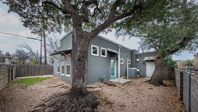 a backyard of a house with large trees and wooden fence