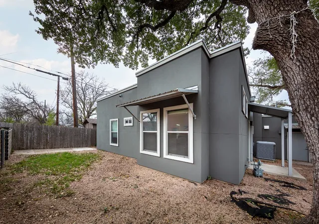 a backyard of a house with large trees and refrigerator