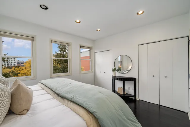 a bedroom with a bed a dresser and potted plants with wooden floor