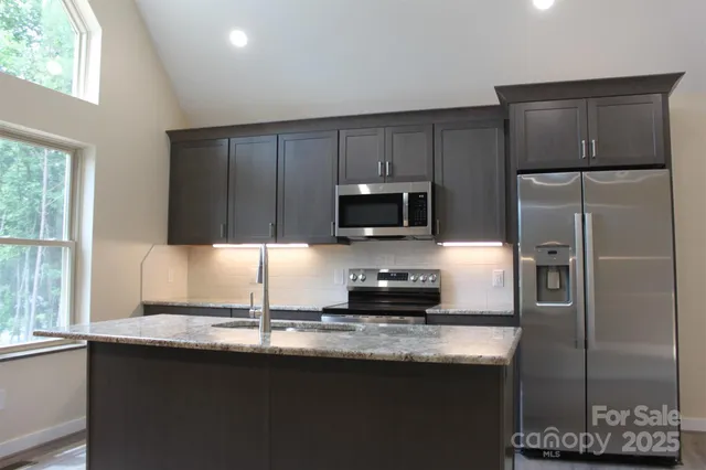 a kitchen with kitchen island granite countertop a refrigerator stove microwave and sink