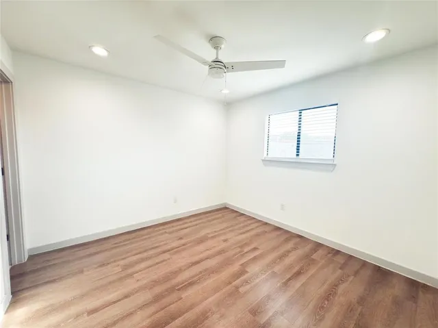 an empty room with wooden floor ceiling fan and windows