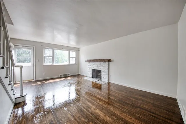 an empty room with wooden floor fireplace and windows