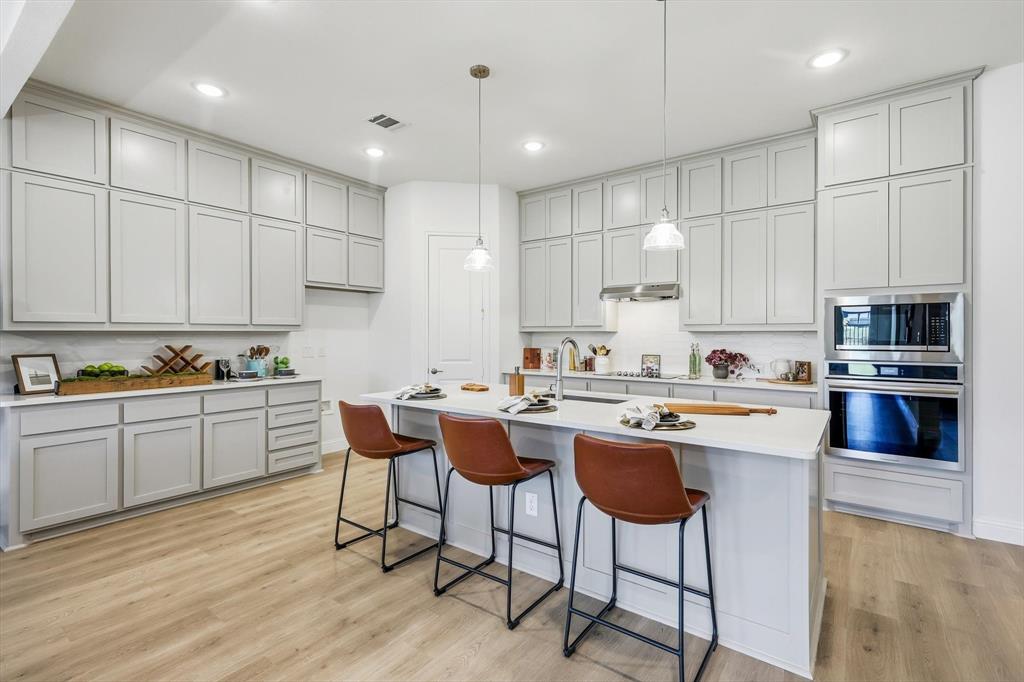 4017 Eagles Bluff Road Midlothian, TX 76065 - Photo 20 of 38 Contemporary kitchen featuring an expansive center island with pendant lighting, light gray cabinetry, built-in stainless steel appliances, white countertops, and wood-finish flooring