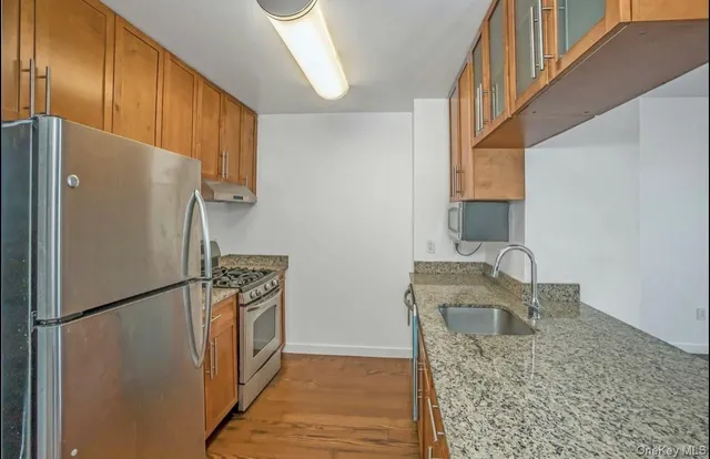 a kitchen with stainless steel appliances granite countertop a refrigerator a stove and a sink with wooden floor