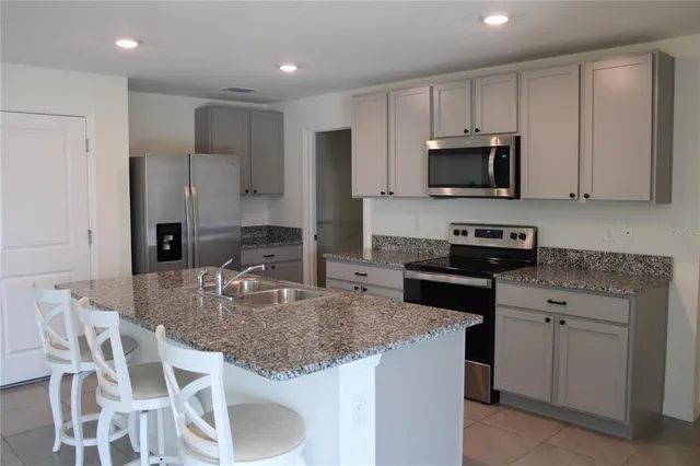 a kitchen with stainless steel appliances granite countertop a stove a sink a microwave a refrigerator and white cabinets