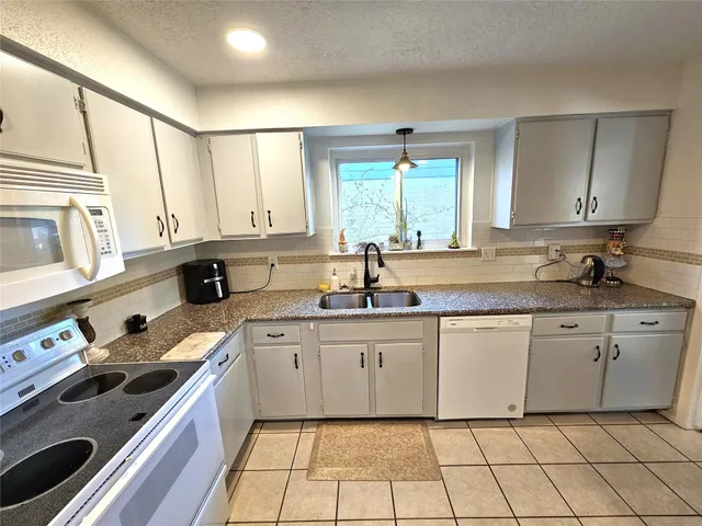a kitchen with granite countertop white cabinets sink and appliances