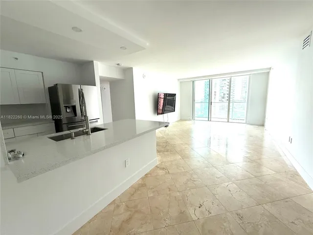 a living room with stainless steel appliances kitchen island granite countertop a rug and a flat screen tv