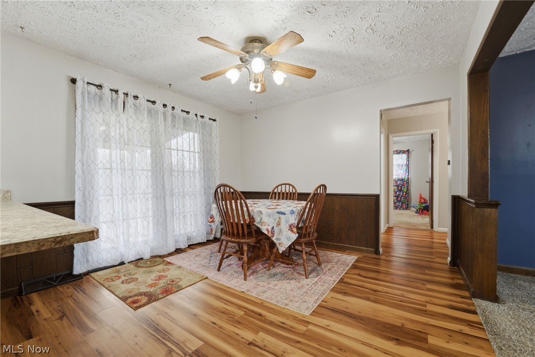 14557 Ellsworth Road Berlin Center, OH 44401 - Photo 11 of 23 Dining room featuring light wood-style floors, a textured ceiling, a ceiling fan, plenty of natural light, and a wainscoted wall