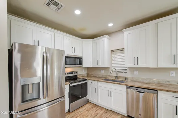 a kitchen with granite countertop a refrigerator sink and white cabinets