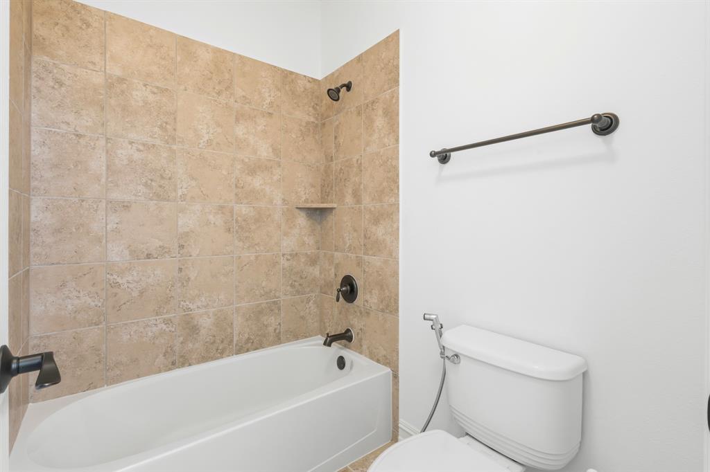 1995 Verde Court Allen, TX 75013 - Photo 8 of 30 Bathroom featuring a white bathtub, bronze fixtures, and light-toned tile surround with an integrated shelf