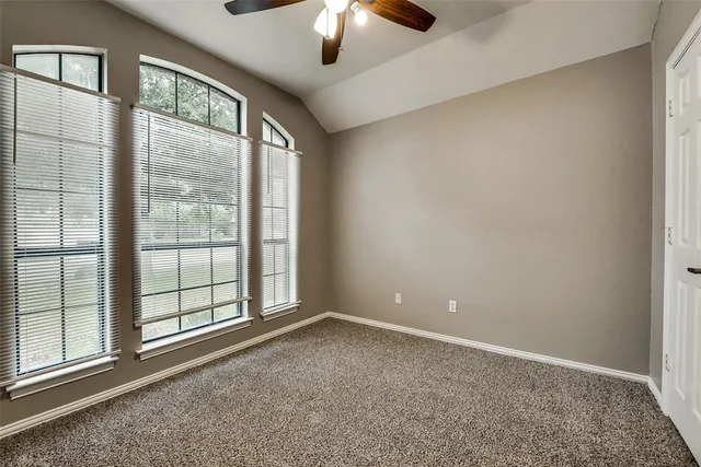 an empty room with chandelier fan and windows