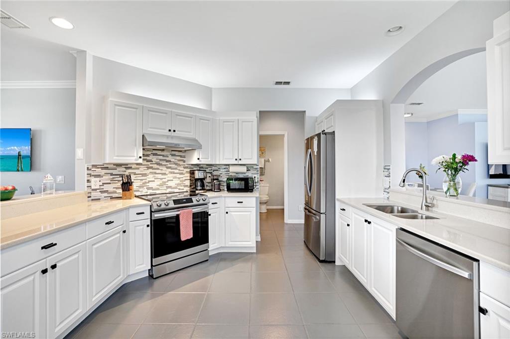 5967 Sand Wedge Lane, Unit 104 Naples, FL 34110 - Photo 6 of 41 a kitchen with white cabinets and stainless steel appliances