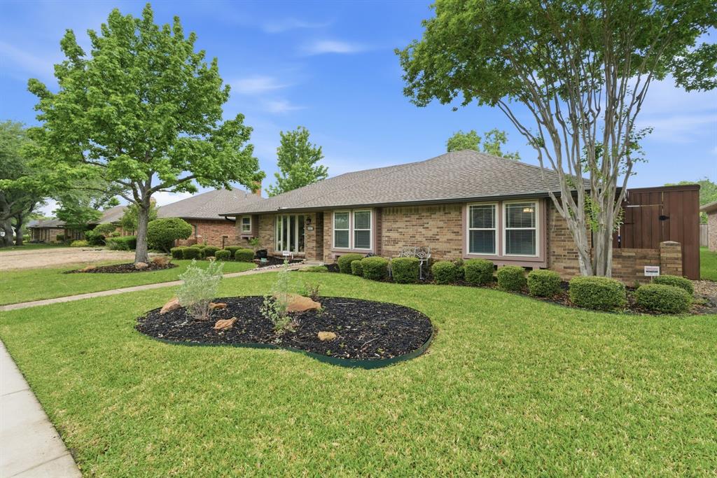 2307 Castle Rock Road Carrollton, TX 75007 - Photo 3 of 34 The property features a brick exterior, a shingle roof, and a well-maintained lawn with mature trees and landscaped beds