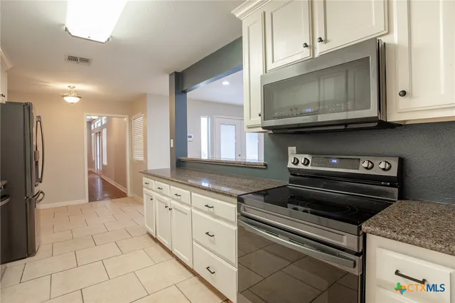 a kitchen with stainless steel appliances granite countertop a stove a microwave and a white cabinets