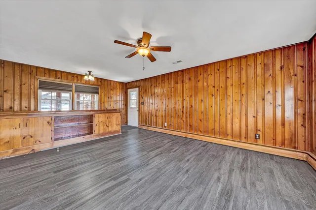 an empty room with wooden floor and windows with curtains
