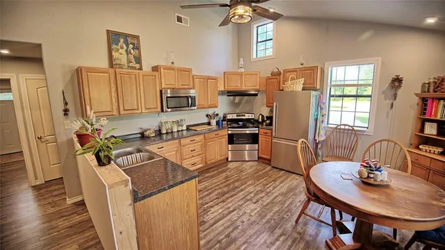 a kitchen with stainless steel appliances granite countertop a stove top oven a sink a dining table and chairs with wooden floor