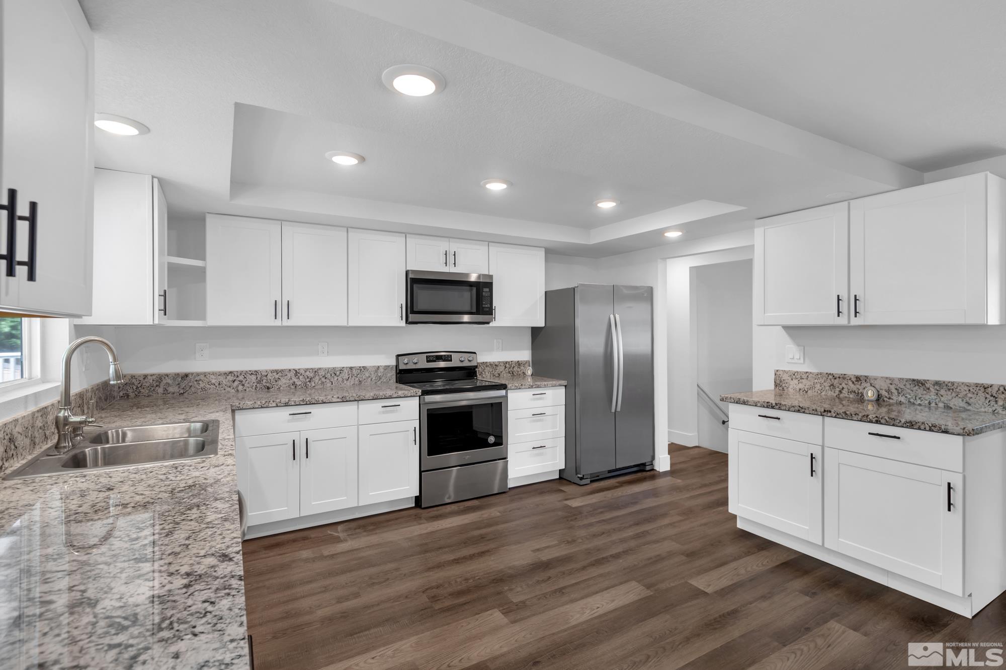 1750 Carlin Street Reno, NV 89503 - Photo 7 of 38 a kitchen with granite countertop a sink stove a refrigerator and white cabinets with wooden floor