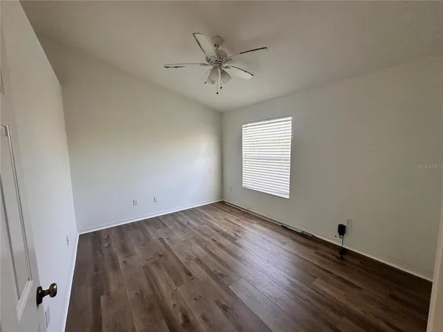 an empty room with wooden floor fan and windows