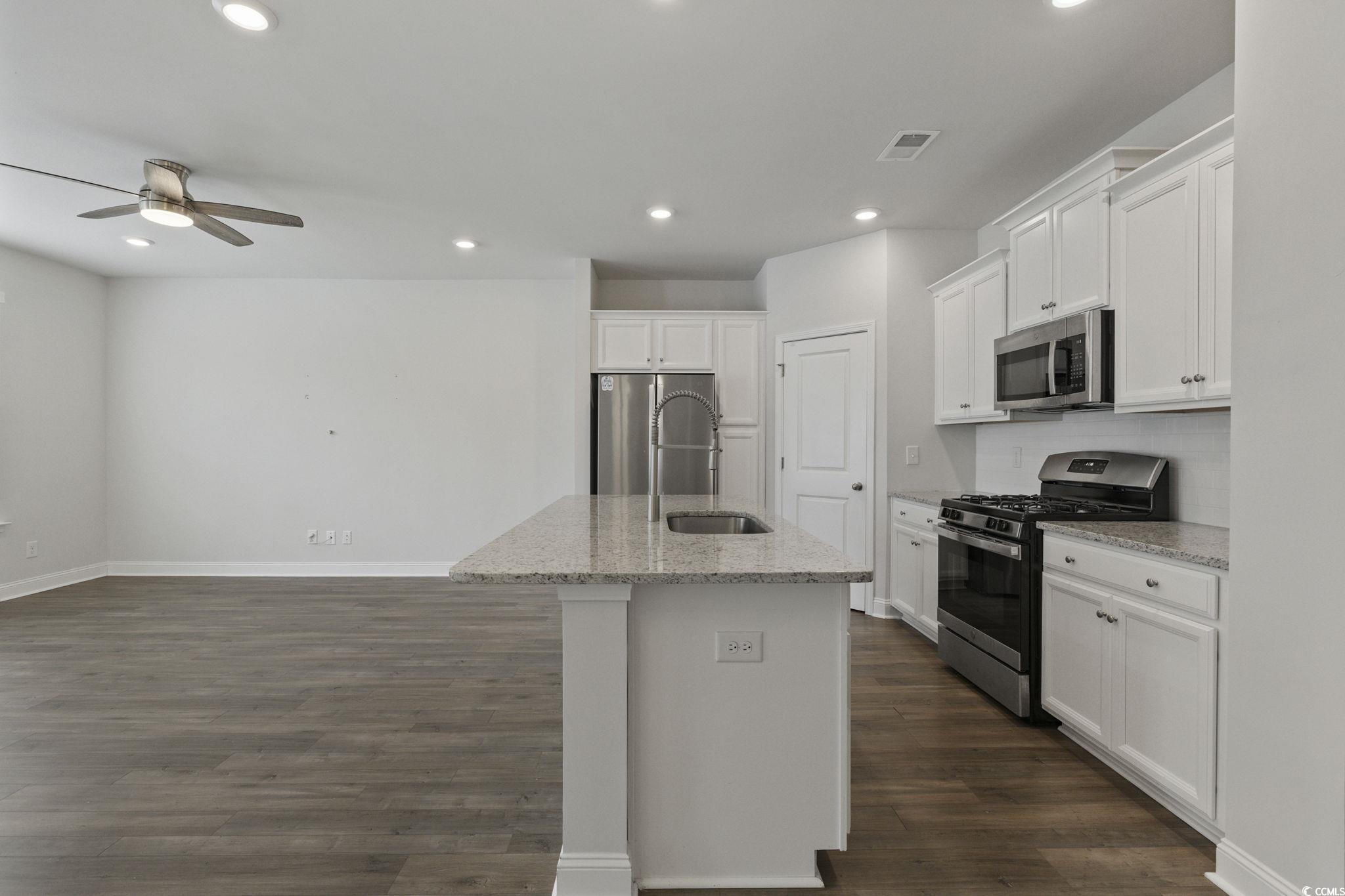 2595 Blue Crane Circle, Unit 102 Myrtle Beach, SC 29577 - Photo 11 of 40 Kitchen featuring white cabinets, appliances with stainless steel finishes, light stone counters, a kitchen island with sink, and dark wood-style flooring