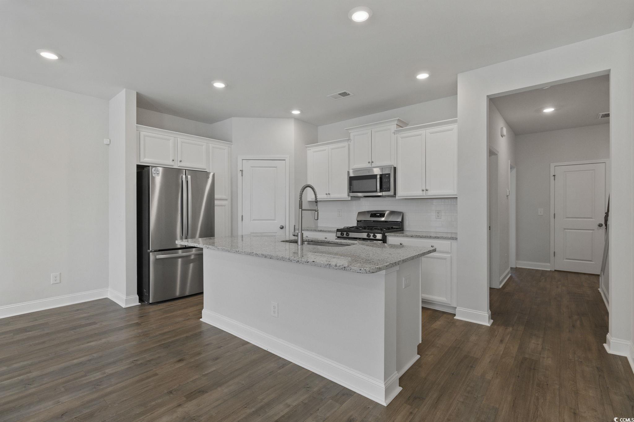 2595 Blue Crane Circle, Unit 102 Myrtle Beach, SC 29577 - Photo 9 of 40 Kitchen with stainless steel appliances, white cabinets, light stone counters, backsplash, and a kitchen island with sink