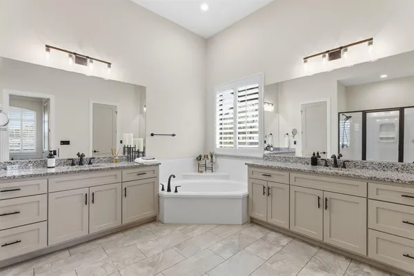 a bathroom with a double vanity sink a mirror a bathtub and next to a window