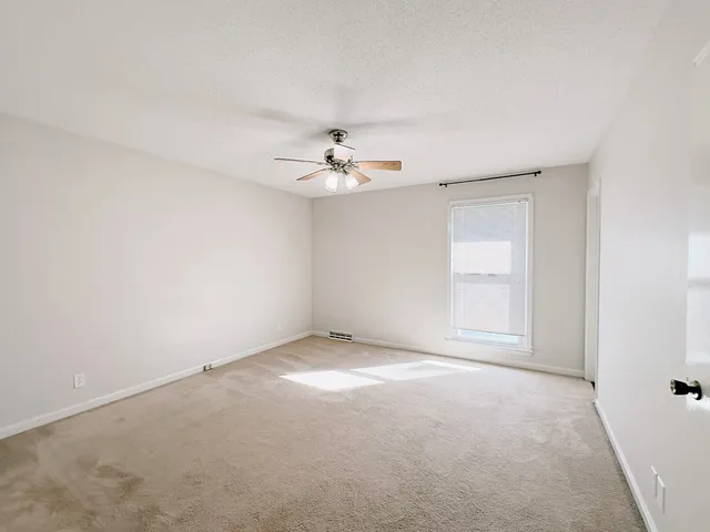 an empty room with chandelier fan and windows