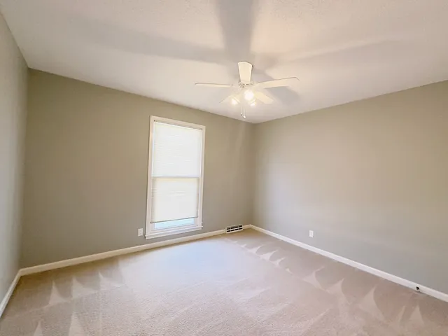 an empty room with a chandelier fan and windows