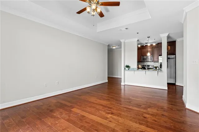 a view of an empty room and kitchen view with wooden floor
