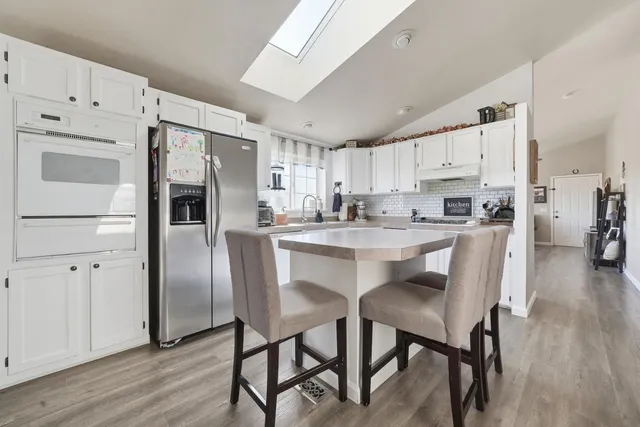 a kitchen with stainless steel appliances a refrigerator a stove a sink and white cabinets with wooden floor